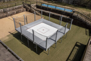 An outdoor trampoline used for fitness and training. Gray, above ground, with safety nets