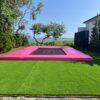 A super trampoline with pink pads and bed marks and a black bed, installed into the ground.